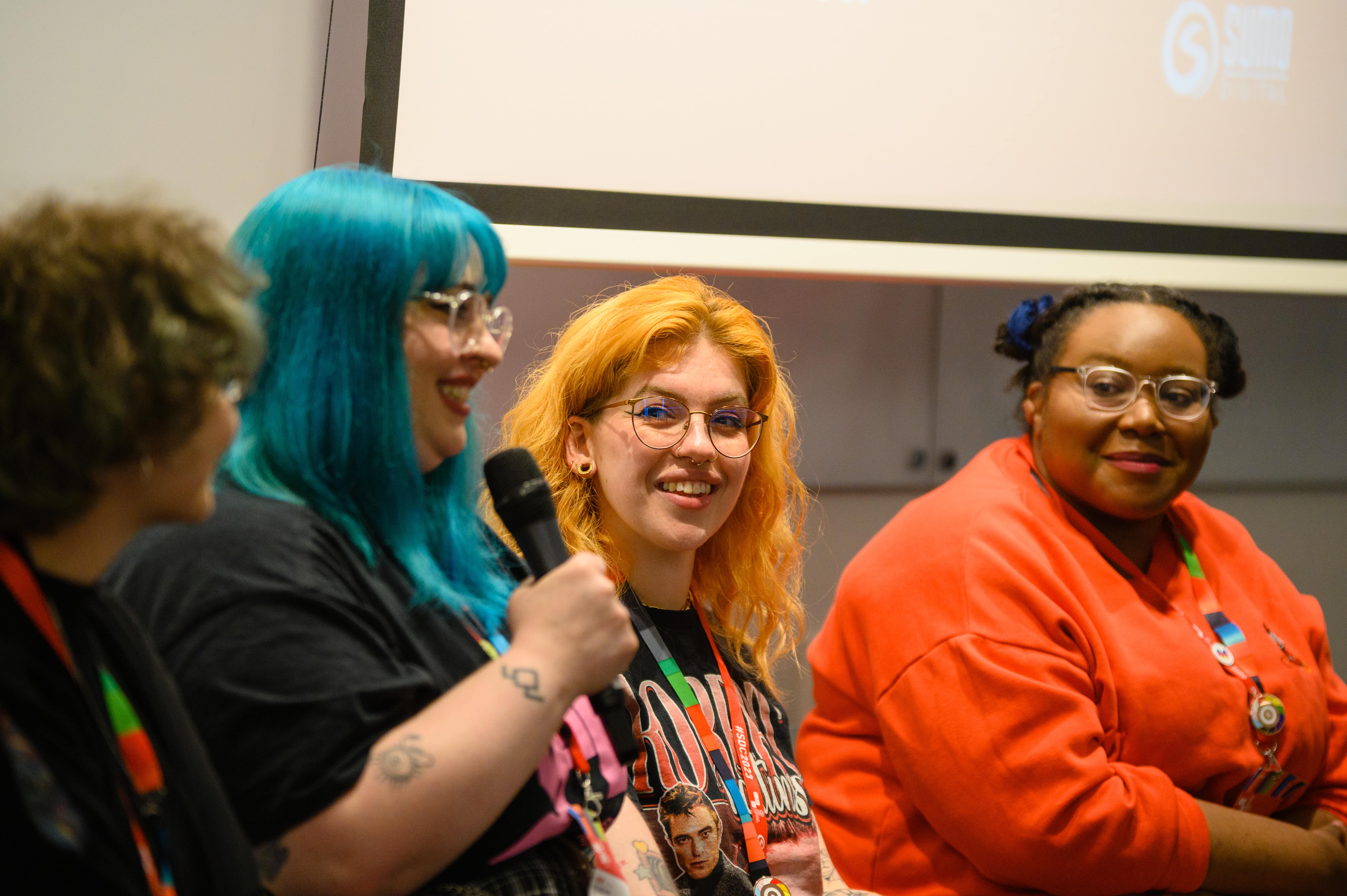 Four people talking at a conference. One holds a microphone and the others look toward them.